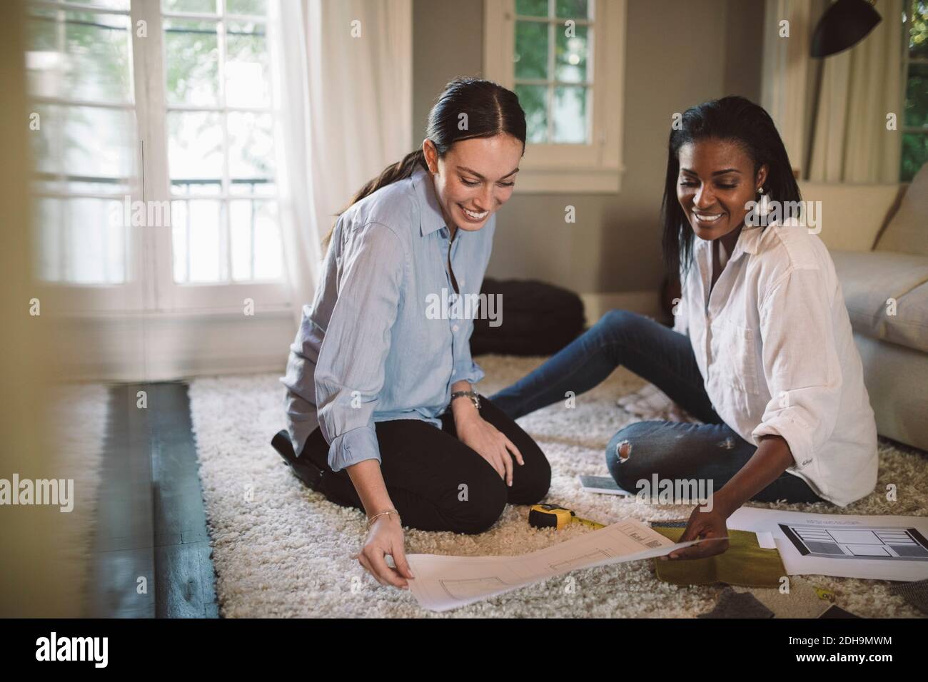 Sorridente designer donne che discutono mentre si siede sul tappeto a casa ufficio Foto Stock