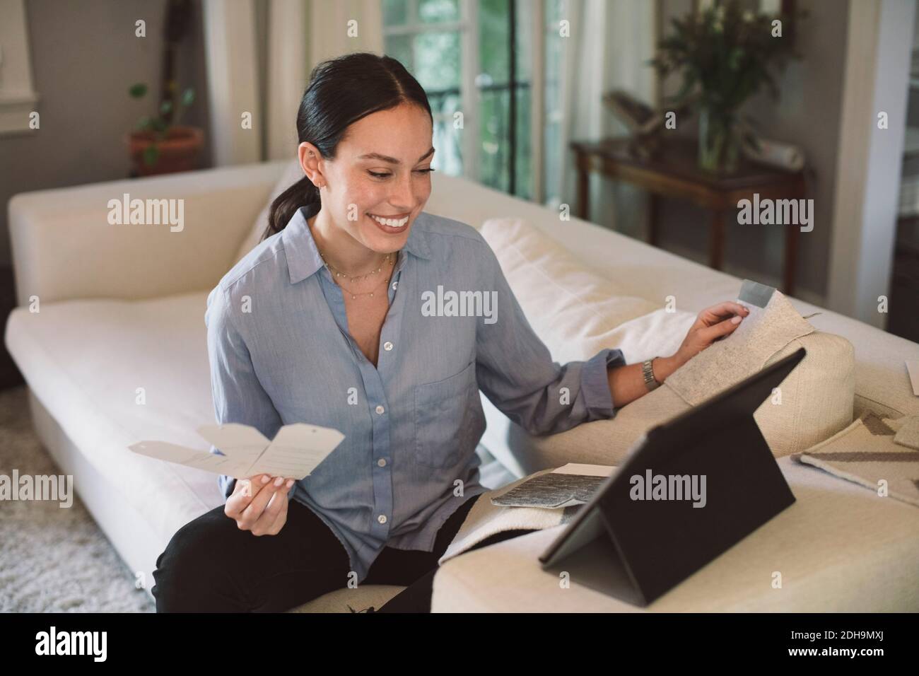 Un designer sorridente che tiene le etichette mentre guarda il notebook a casa ufficio Foto Stock