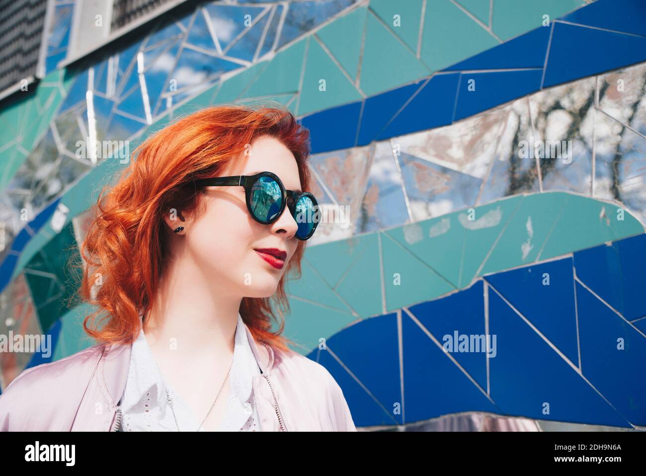 Giovane donna rossa che indossa occhiali da sole contro la parete del mosaico Foto Stock
