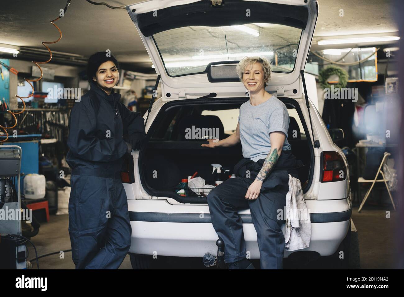 Ritratto di sorridente meccanica femminile con vano auto aperto a. officina di riparazione automatica Foto Stock