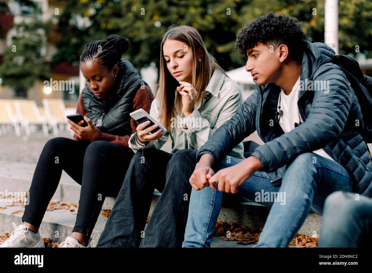 Ragazze adolescenti che usano lo smartphone mentre si siedono con un amico passi in città Foto Stock