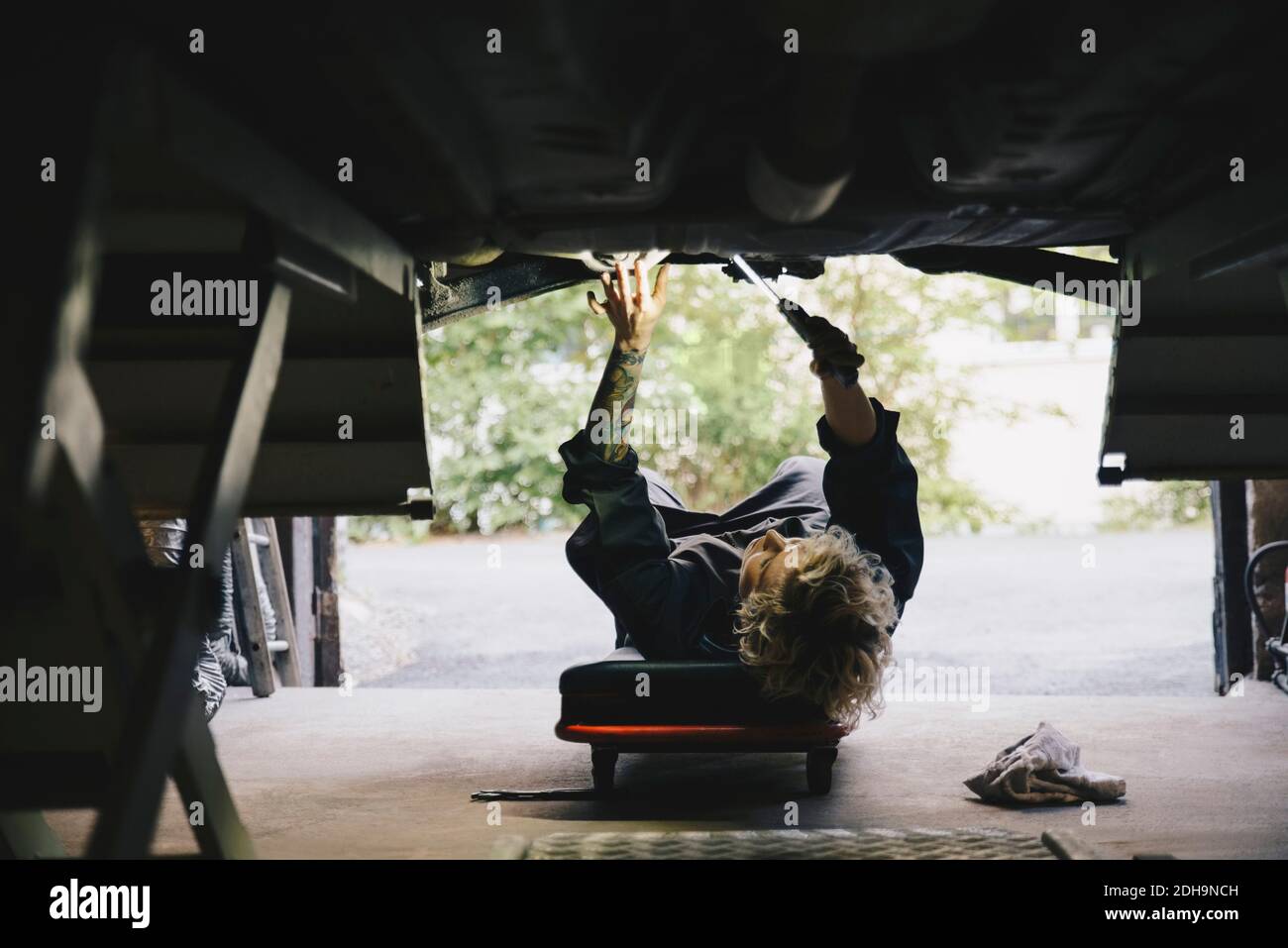 Vista dal basso del meccanico femminile che ripara l'auto presso l'officina di riparazione Foto Stock