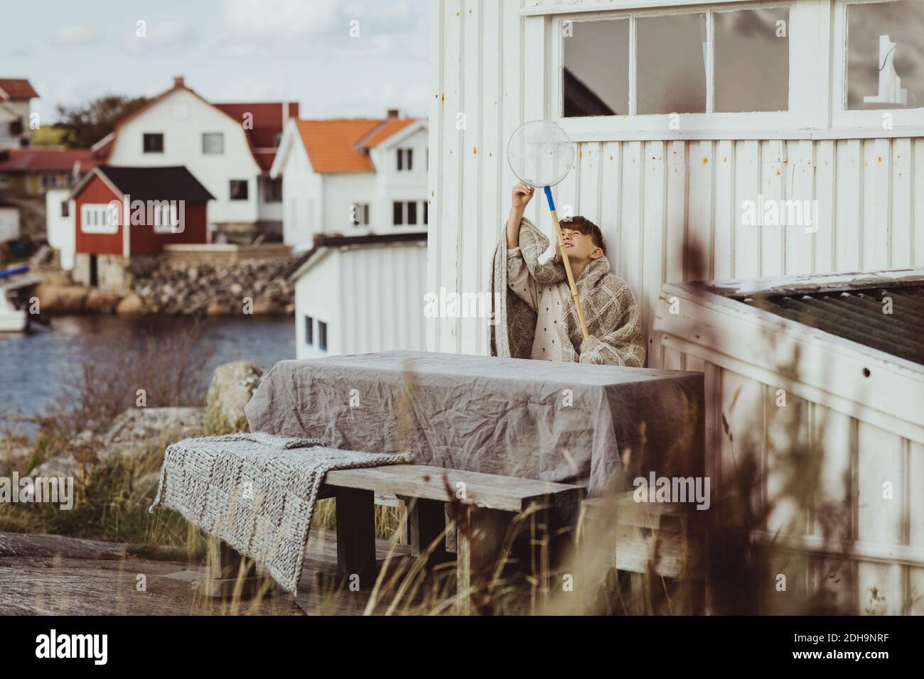 Ragazzo con rete da pesca seduto mentre indossa coperta contro la cabina Foto Stock