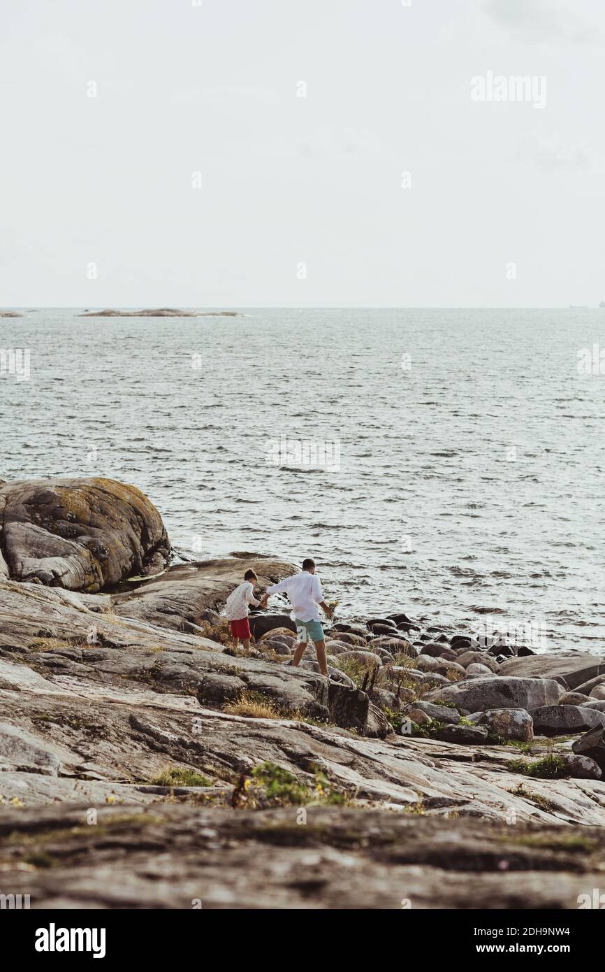 Vista posteriore del padre con il figlio che cammina verso il mare terra rocciosa contro il cielo Foto Stock