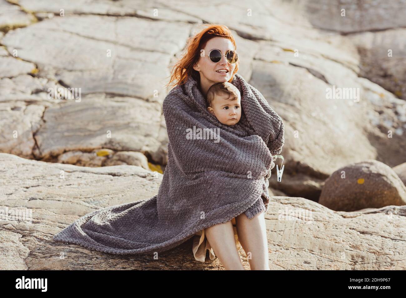 Madre e bambina avvolti in coperta mentre si siedono formazione rocciosa durante l'estate Foto Stock