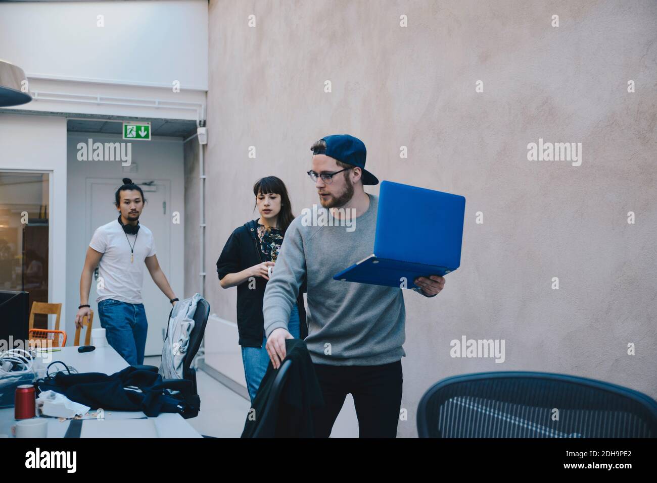 Programmatore di computer che tiene un computer portatile mentre si cammina con i colleghi in ufficio Foto Stock