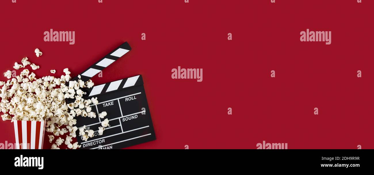 Guardare film con popcorn e clapperboard su sfondo rosso. Accessori per film, concetto cinematografico. Striscione lungo e largo con spazio per la copia Foto Stock