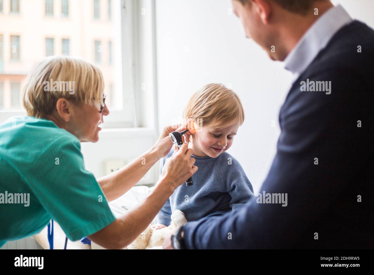 Dottoressa che esamina l'orecchio del ragazzo con otoscopio mentre si siede padre in ospedale Foto Stock