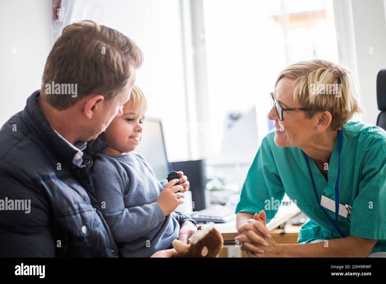 Sorridente medico maturo che parla con il padre in clinica Foto Stock