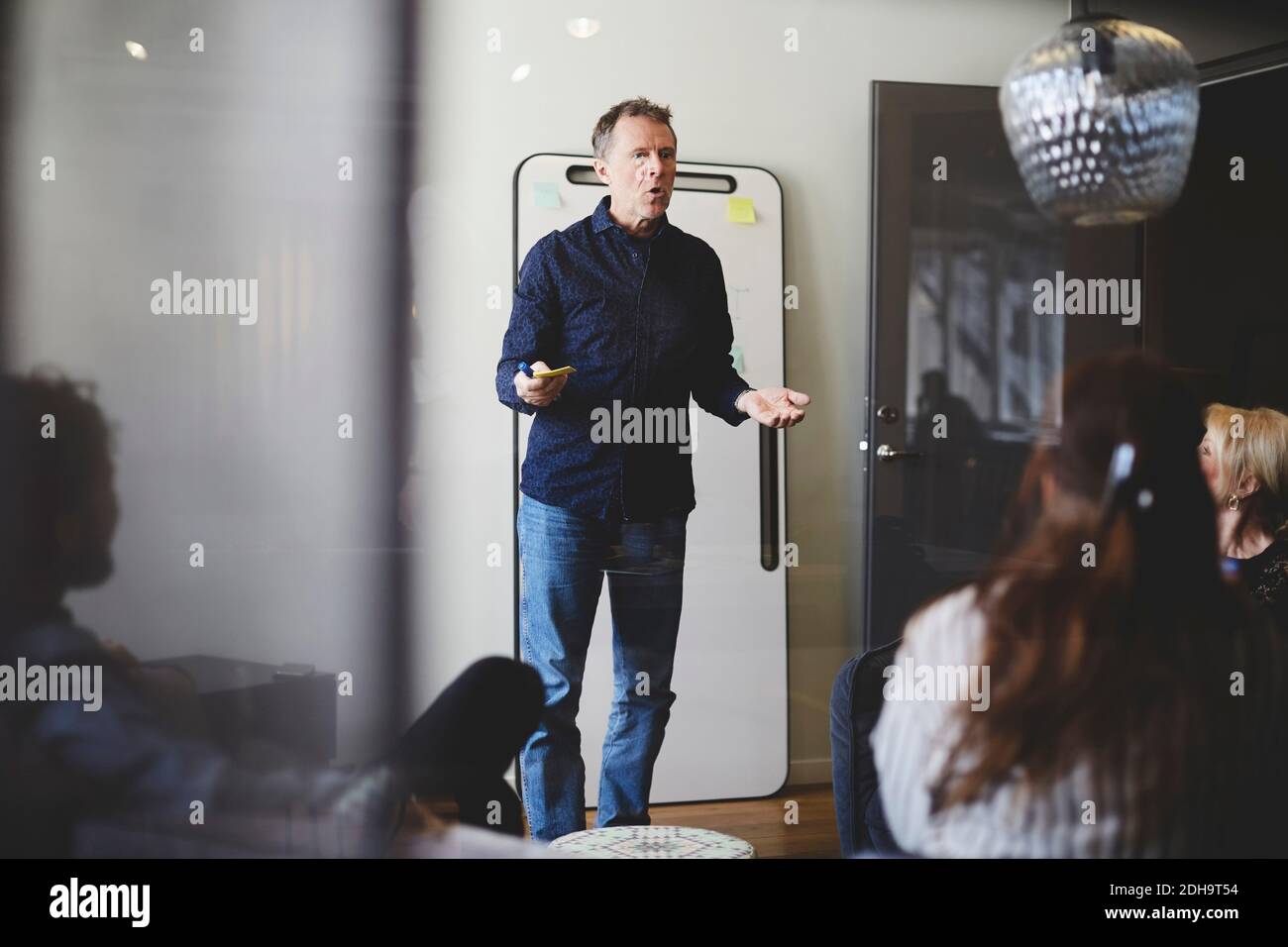 Uomo d'affari maturo che dà la presentazione ai colleghi in sala visto dal vetro Foto Stock