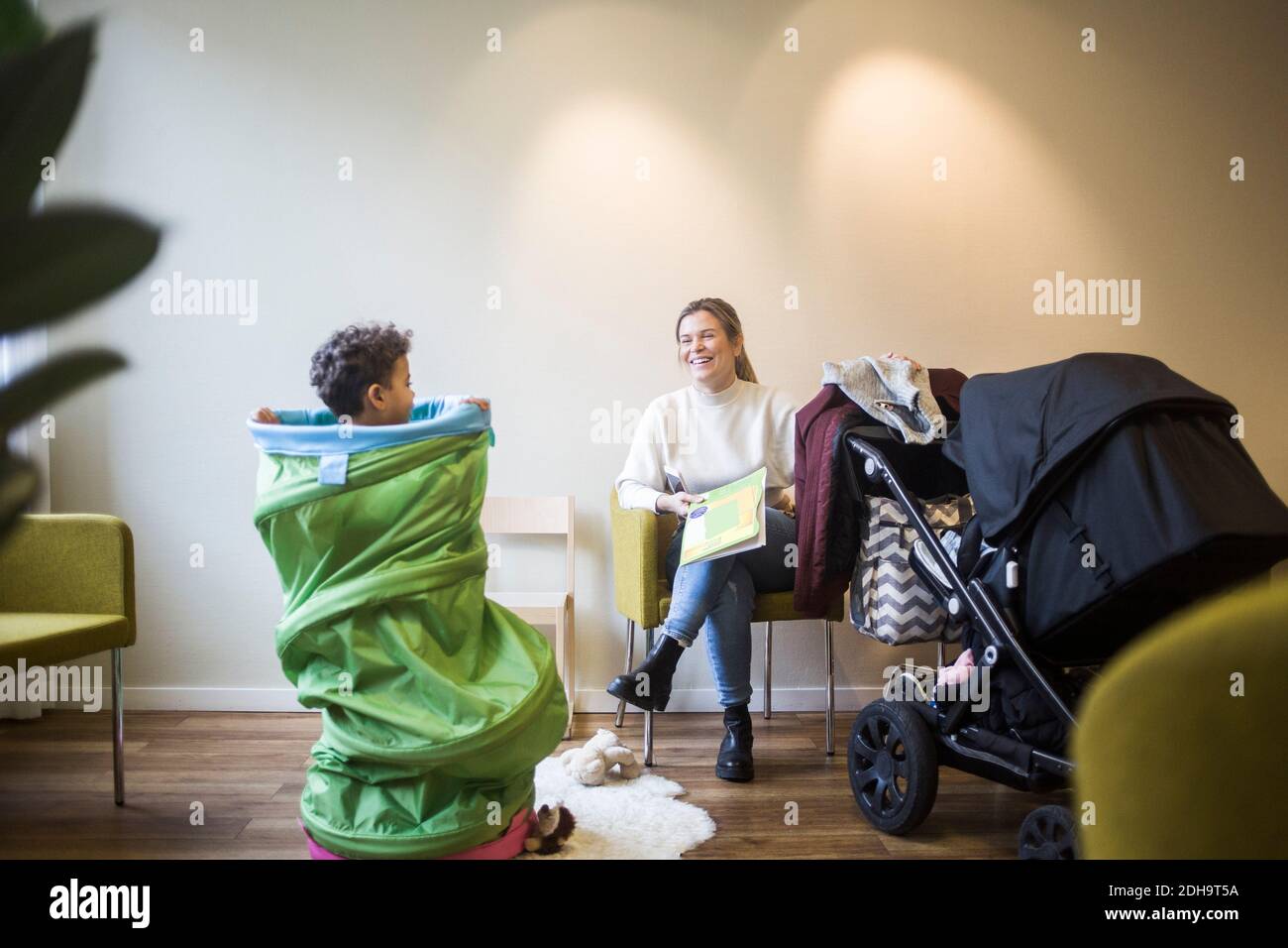 Madre sorridente che guarda il figlio che gioca con le attrezzature del tunnel dentro ospedale Foto Stock