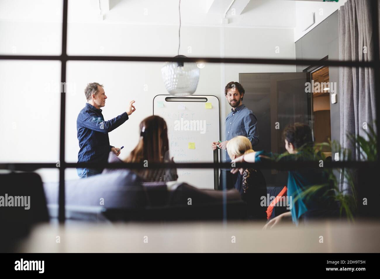 Vista ad angolo basso dei professionisti maschili che danno la presentazione alle donne i colleghi sono stati visti dal vetro nella sala riunioni del creative Foto Stock