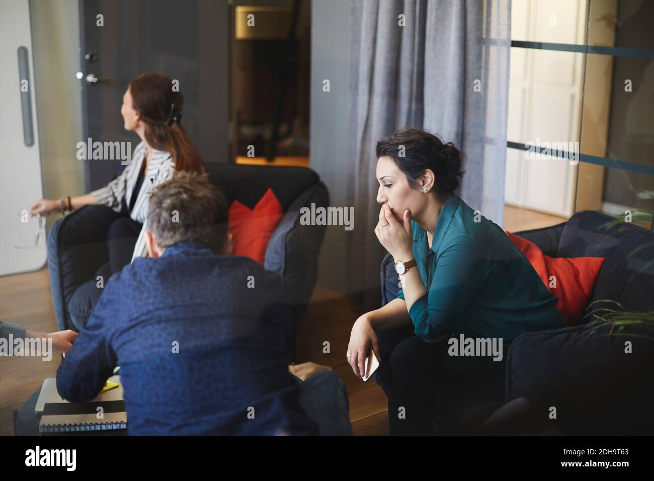 Professionisti seduti nella sala riunioni durante la riunione in ufficio creativo visto dal vetro Foto Stock