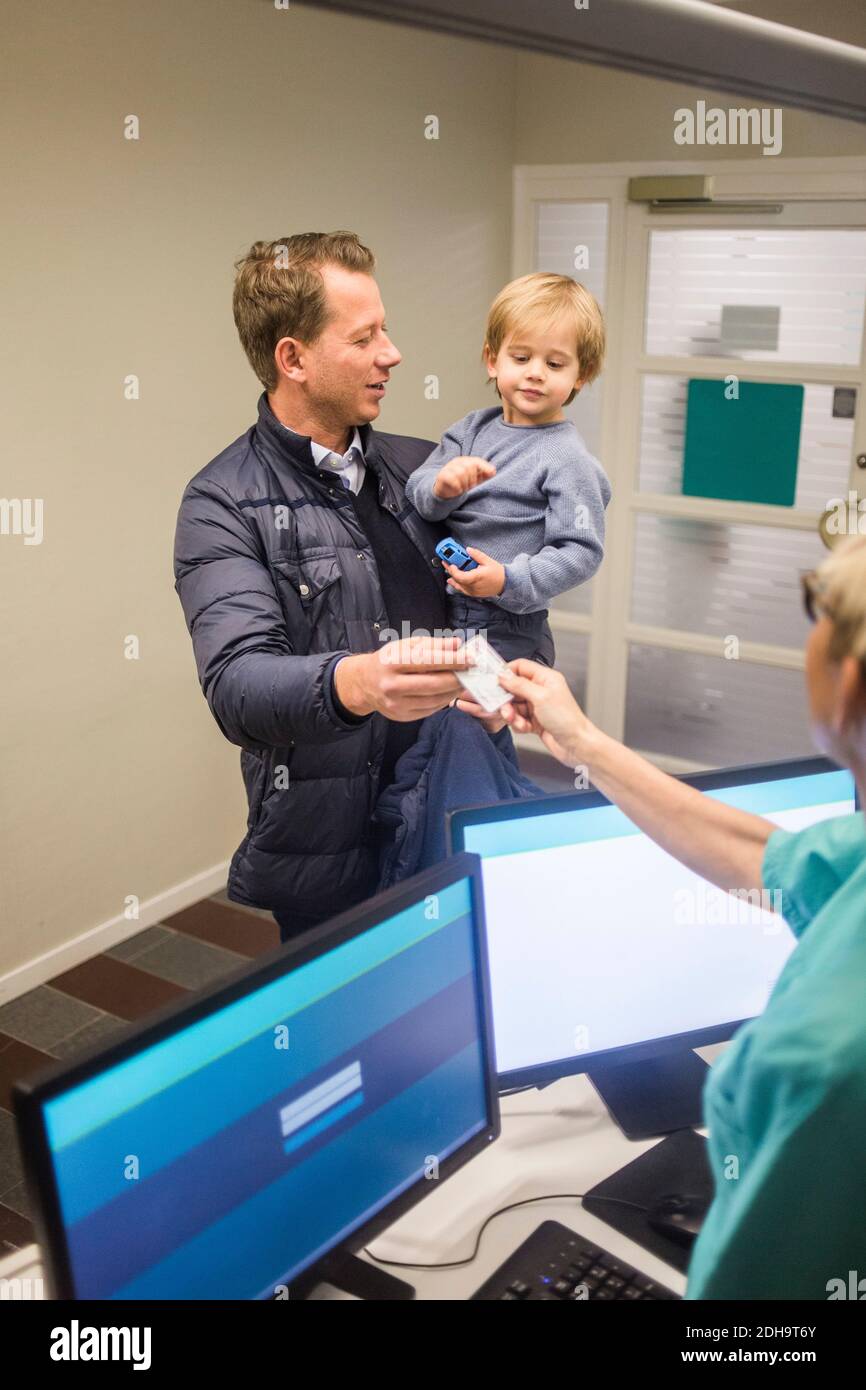 Uomo maturo che dà carta d'identità al medico femminile durante il trasporto figlio in ospedale Foto Stock