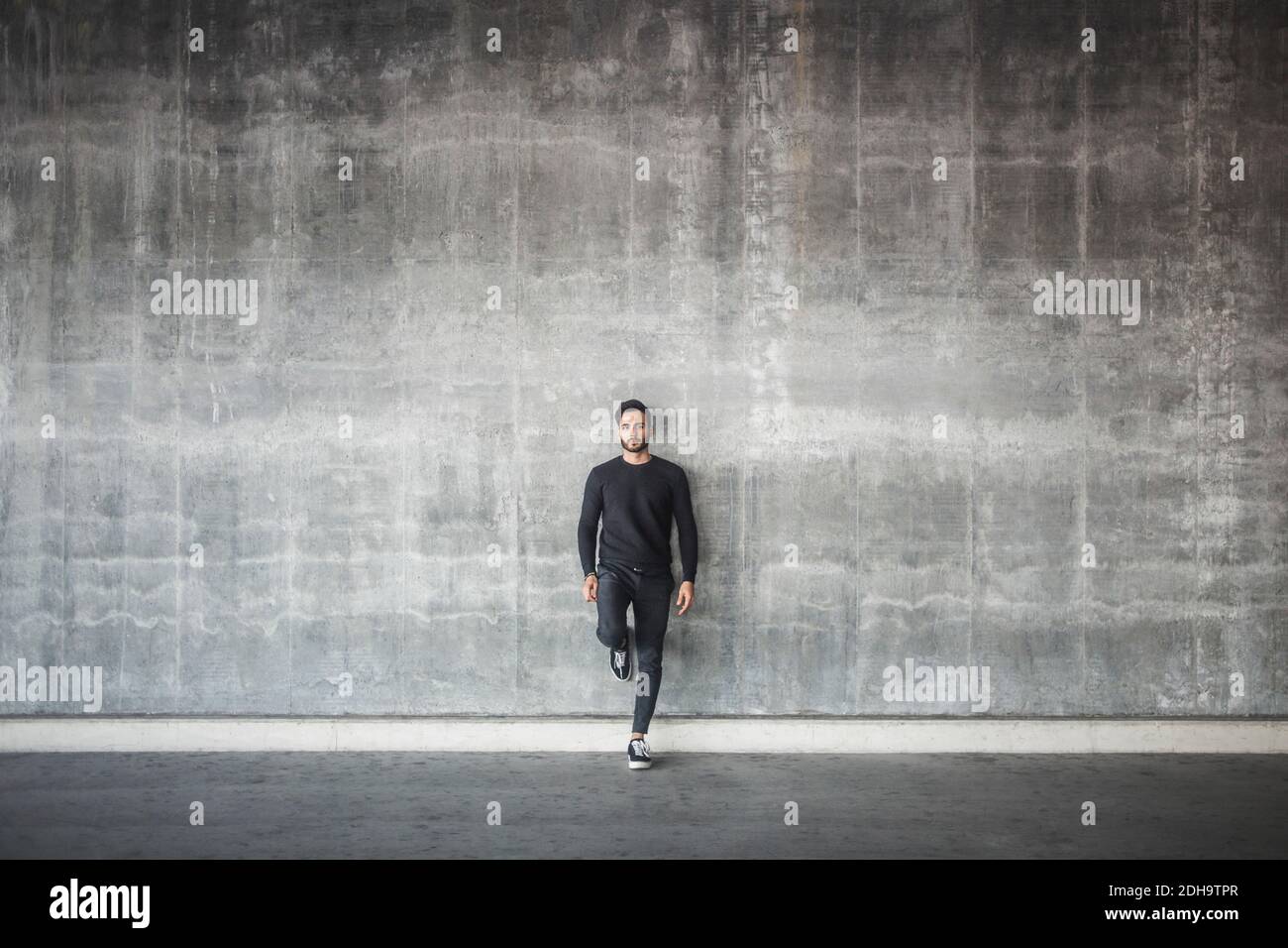 Ritratto di giovane uomo in piedi contro parete grigia Foto Stock