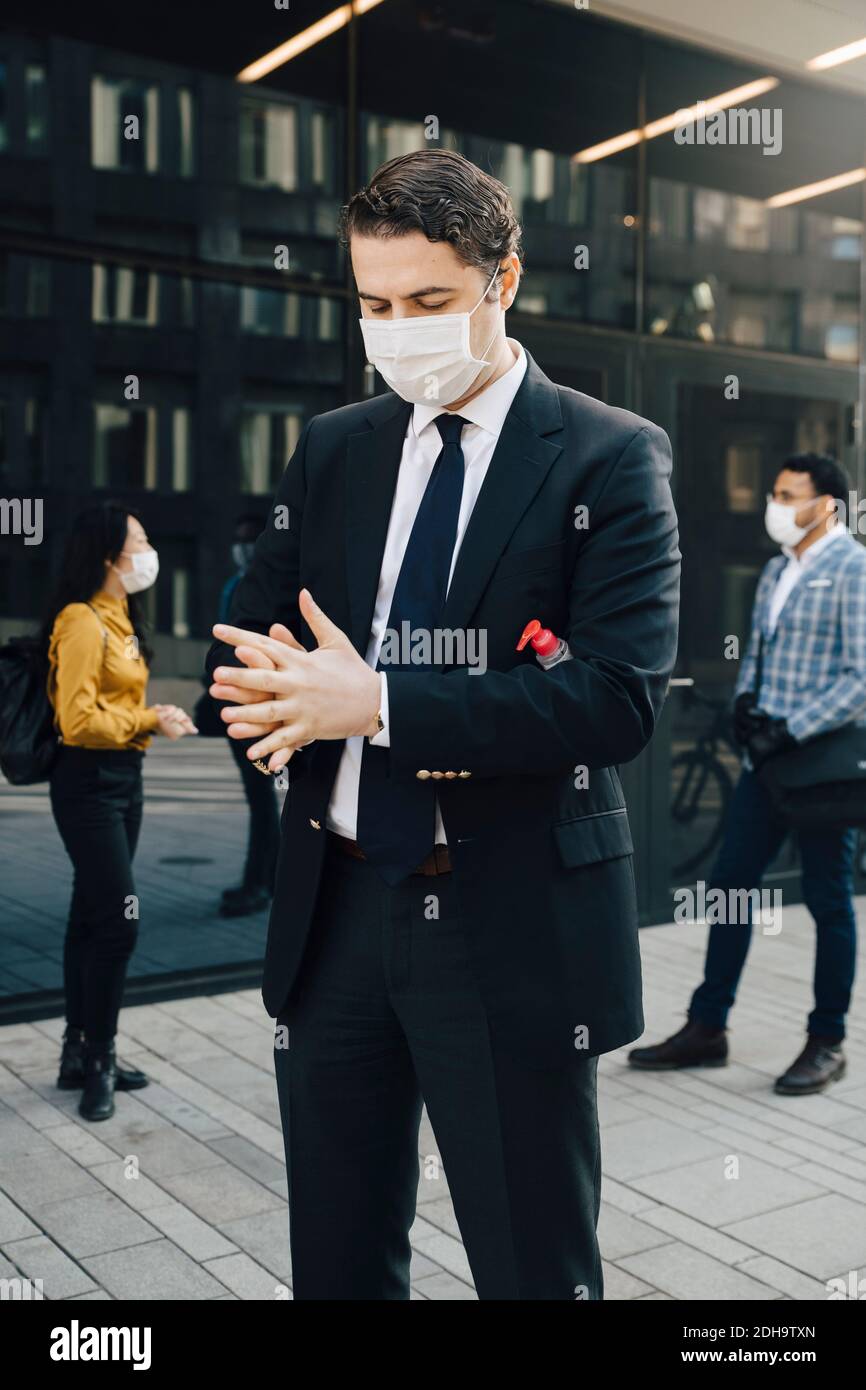 Uomo d'affari con maschera viso lavando le mani con disinfettante per le mani Foto Stock