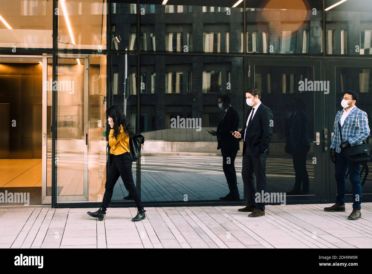 Uomini d'affari con maschere in piedi in linea fuori ufficio edificio Foto Stock