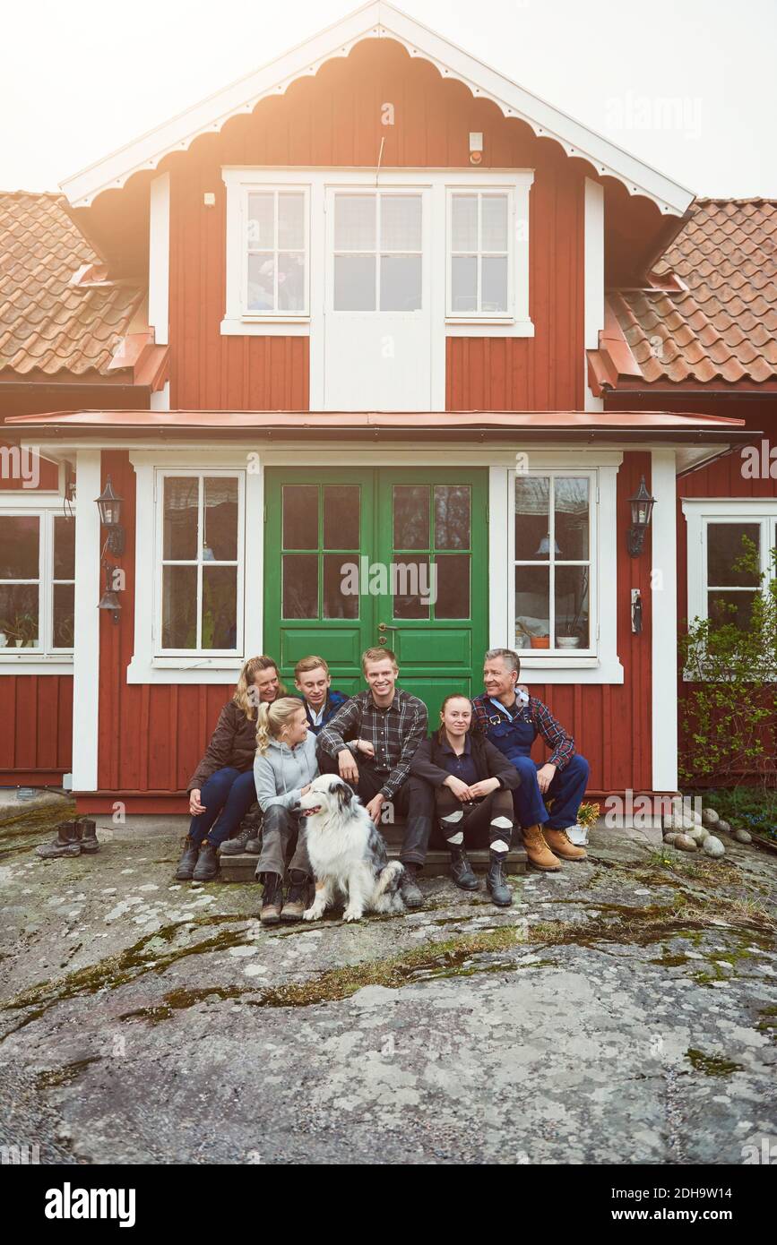 Famiglia sorridente seduto con animale domestico all'ingresso della casa Foto Stock