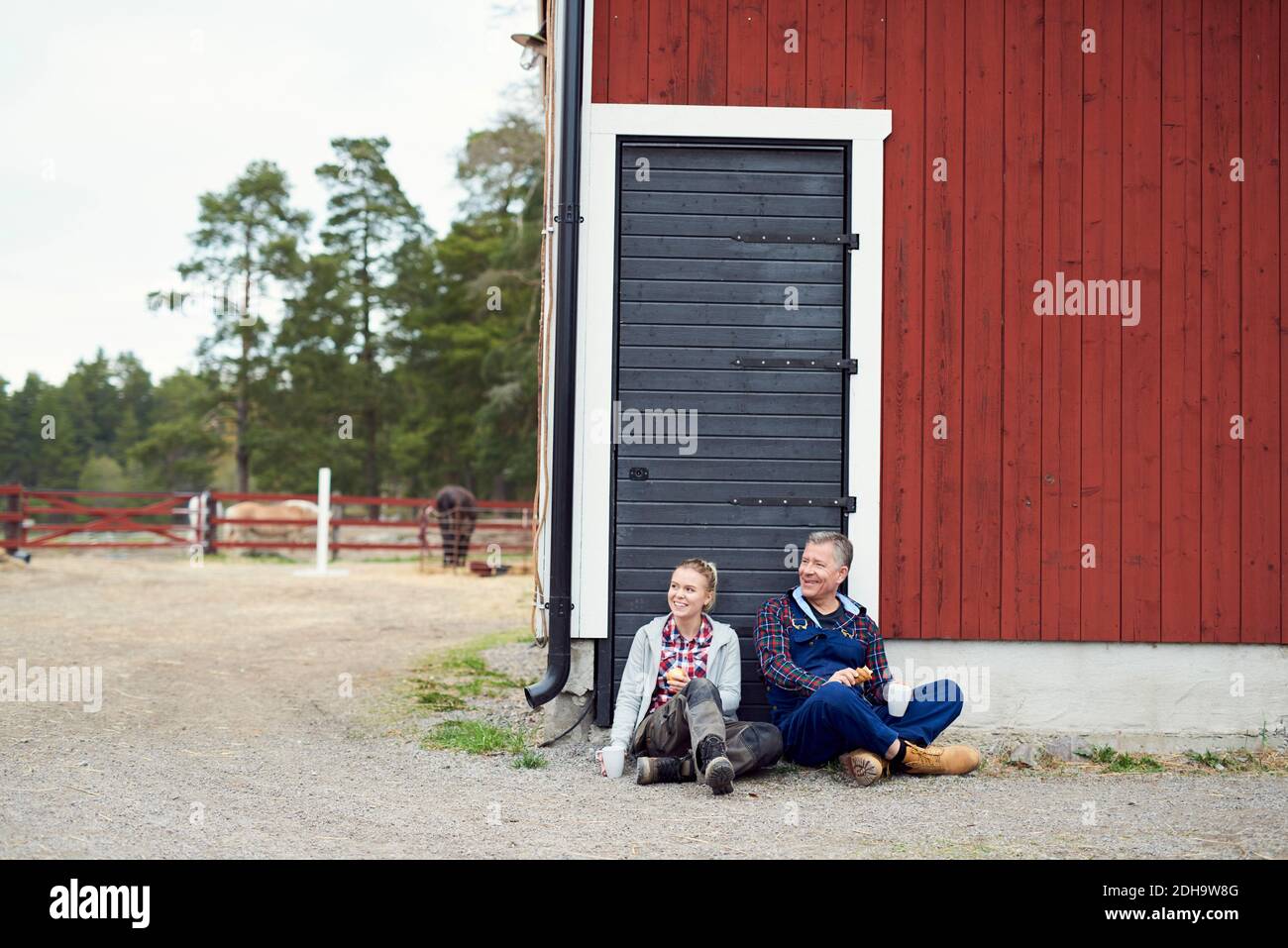 Sorridente contadino e figlia che guardano via mentre si siedono contro il fienile Foto Stock