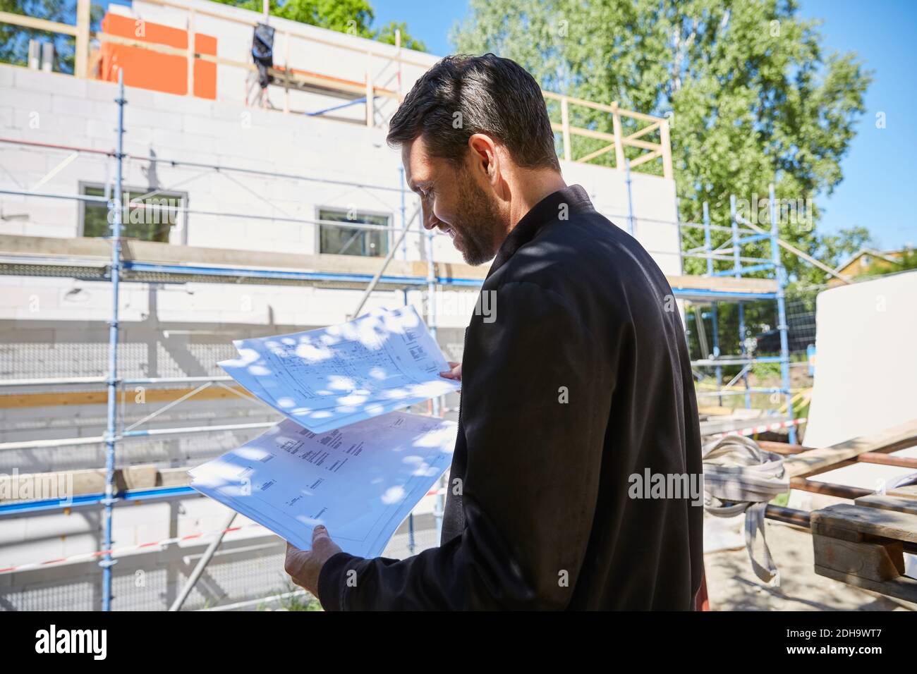 Uomo d'affari che legge i progetti mentre sta in piedi al luogo di costruzione sul sole giorno Foto Stock