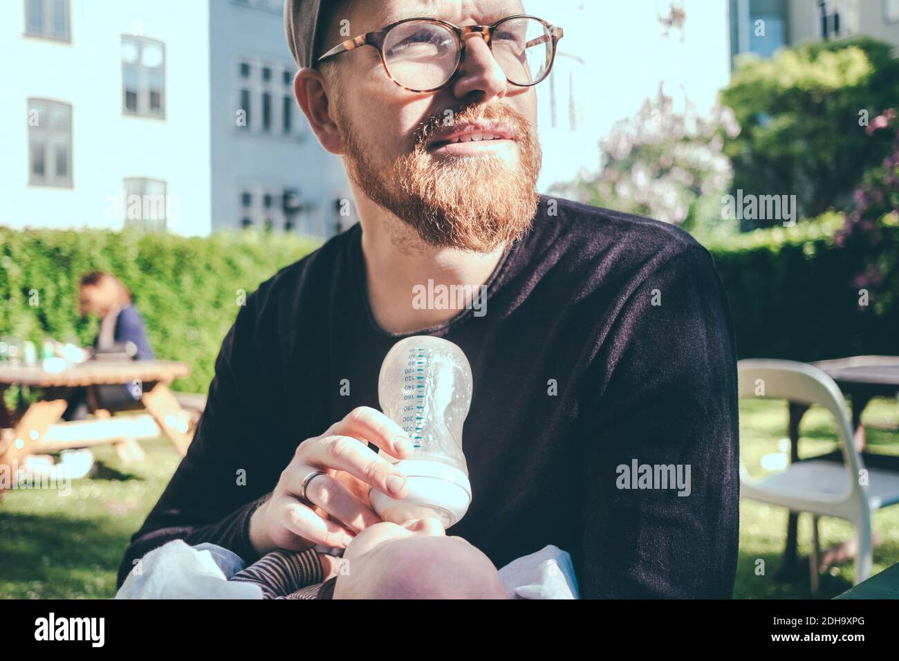 Uomo medio adulto che guarda via mentre allatta il latte dal biberon al bambino al parco Foto Stock