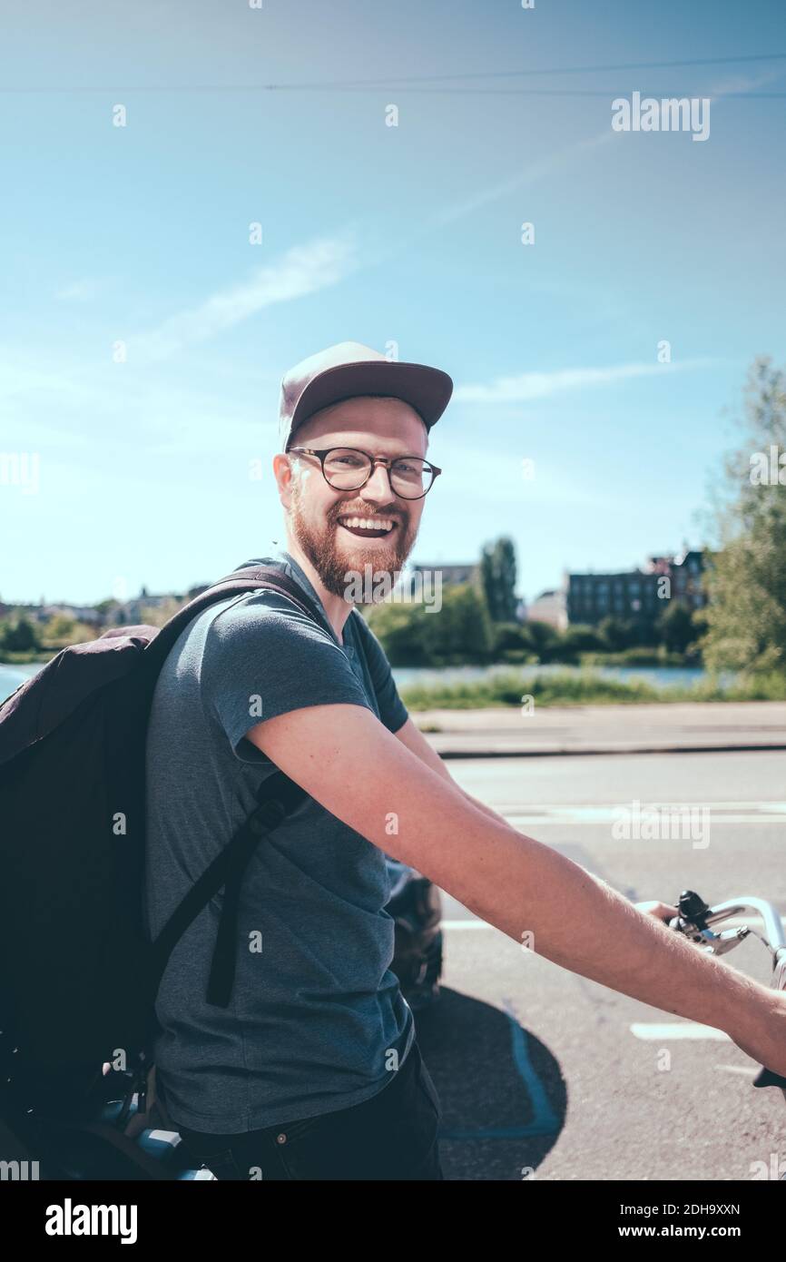 Ritratto con vista laterale dello zaino da trasporto dell'uomo felice durante la guida bicicletta sulla strada contro il cielo Foto Stock