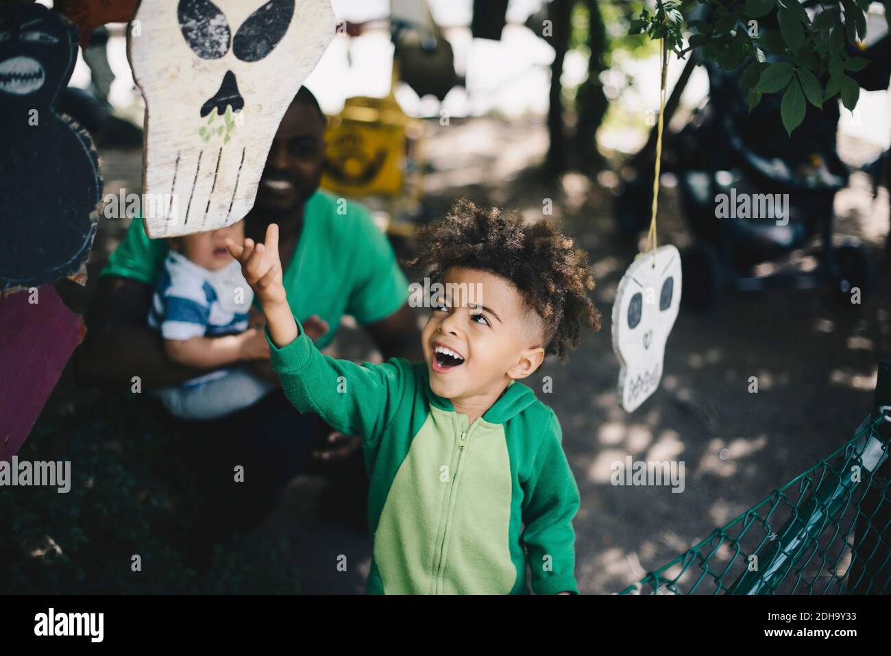 Felice ragazzo che arriva per appendere decorazione con padre e fratello in background Foto Stock