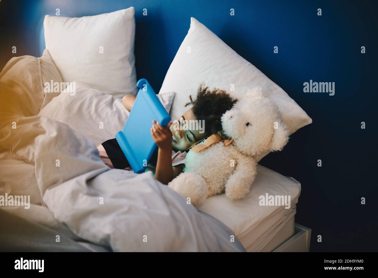 Vista ad alto angolo del ragazzo sdraiato con giocattolo imbottito mentre utilizzo di un tablet digitale a letto a casa Foto Stock Vista ad alto angolo del ragazzo sdraiato con giocattolo imbottito mentre utilizzo di un tablet digitale a letto a casa Foto Stock