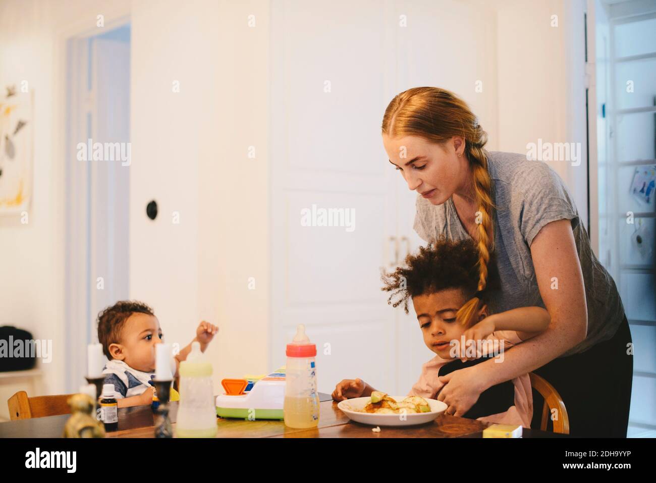 Bambino che guarda la madre che dà cibo al fratello a casa Foto Stock