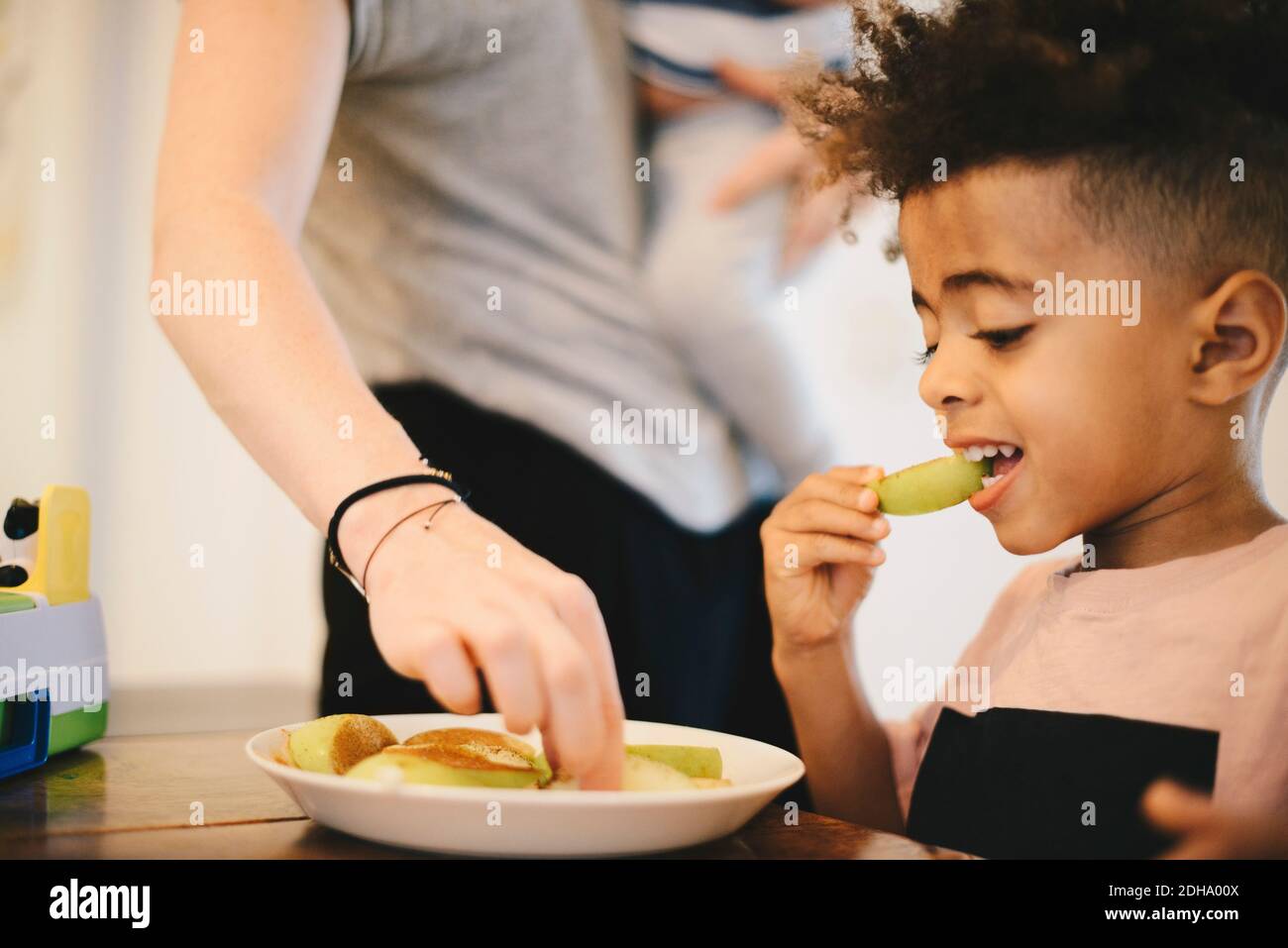 Ragazzo che ha cibo mentre si siede da madre a casa Foto Stock