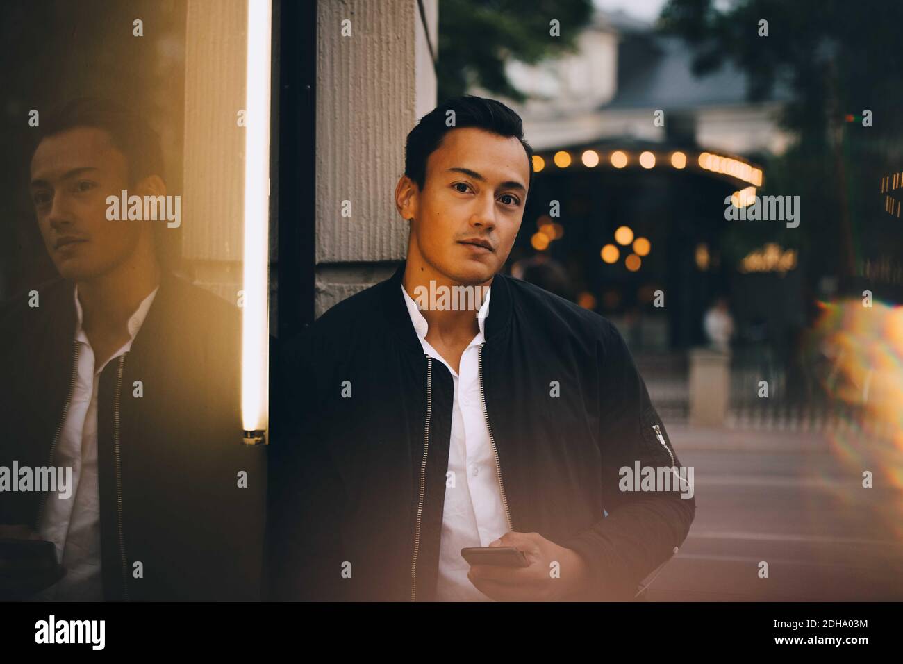 Ritratto di giovane uomo con telefono in piedi in città Foto Stock