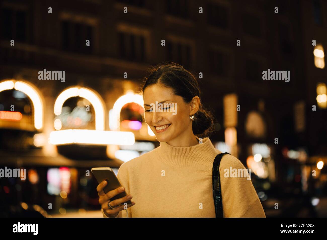Donna sorridente che si sta testando attraverso il cellulare mentre si trova in città a. notte Foto Stock