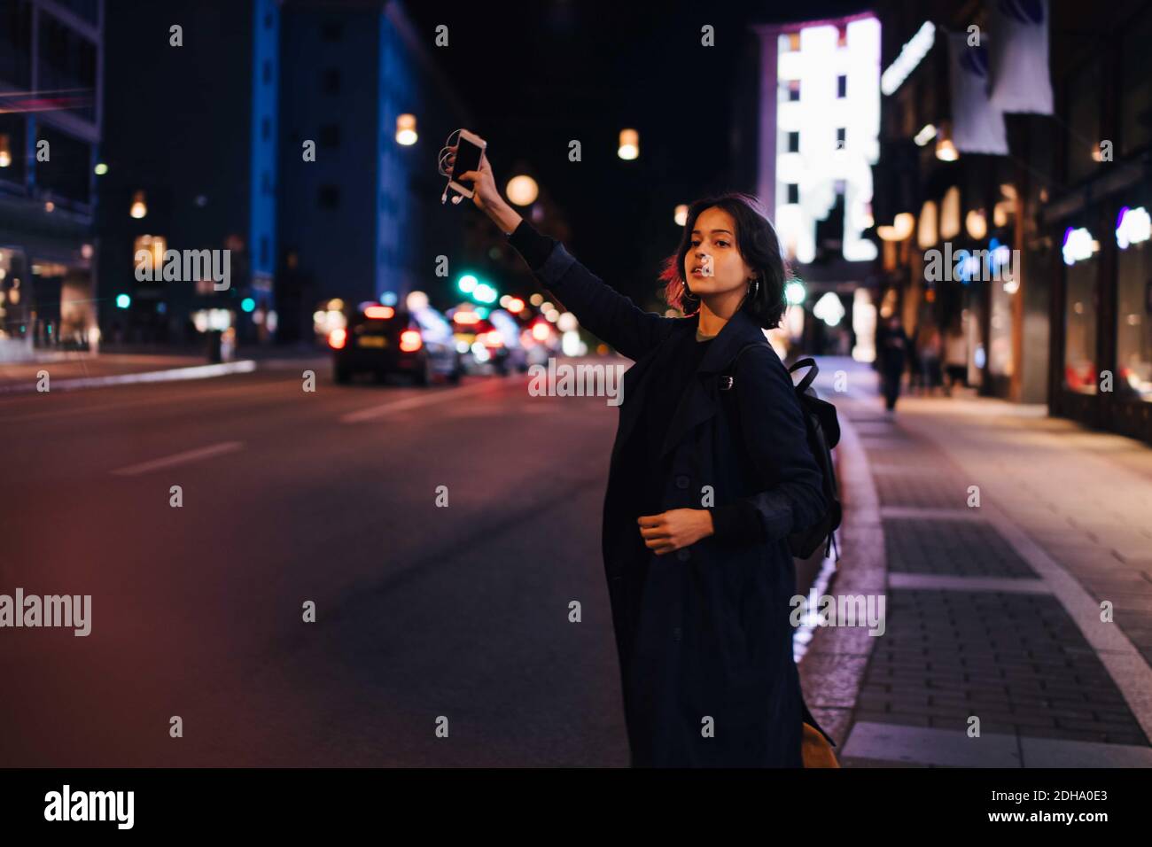 Giovane donna con telefono in arrivo per taxi in città a. notte Foto Stock