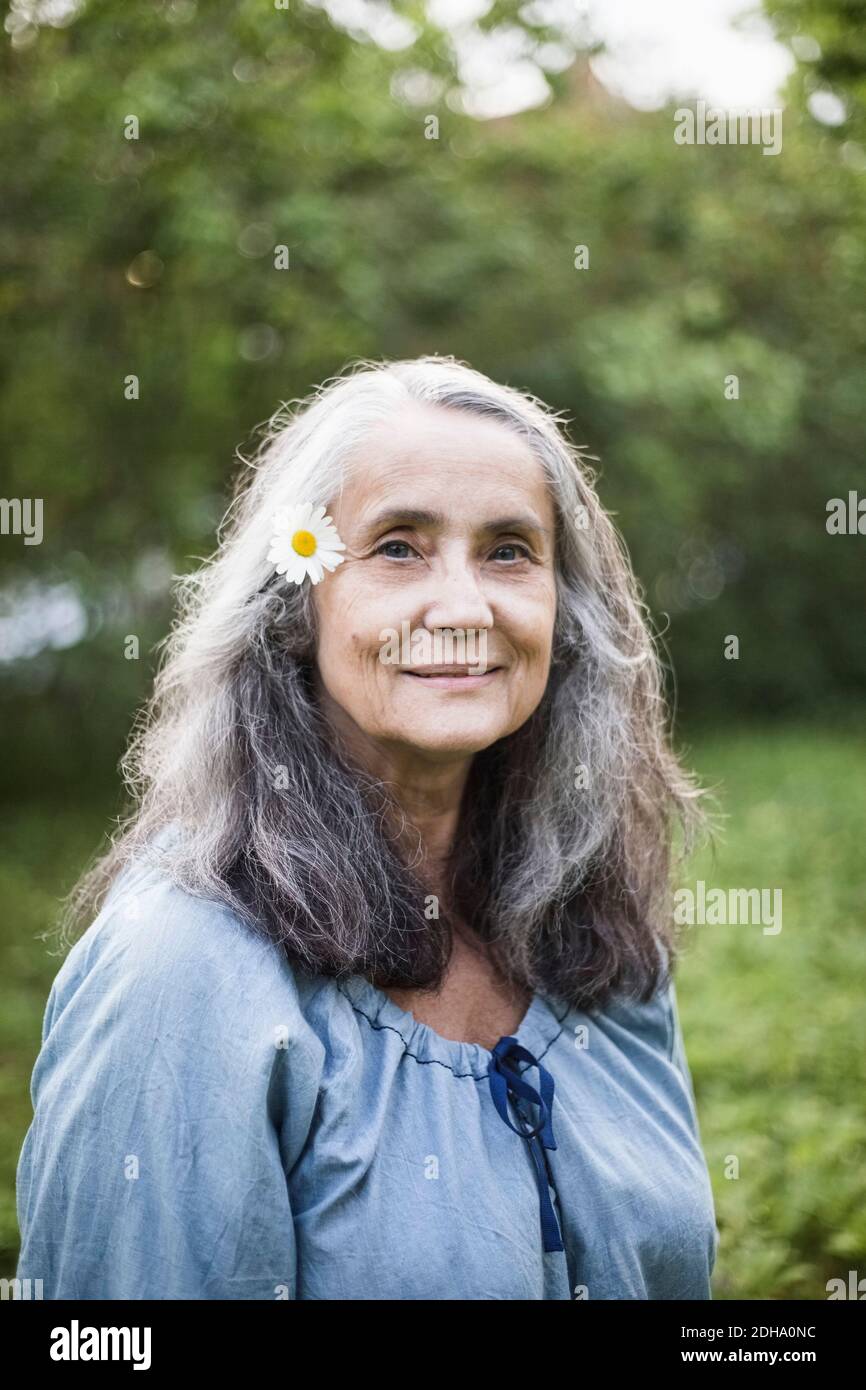 Ritratto di donna anziana sorridente con fiore a margherita sul retro iarda Foto Stock