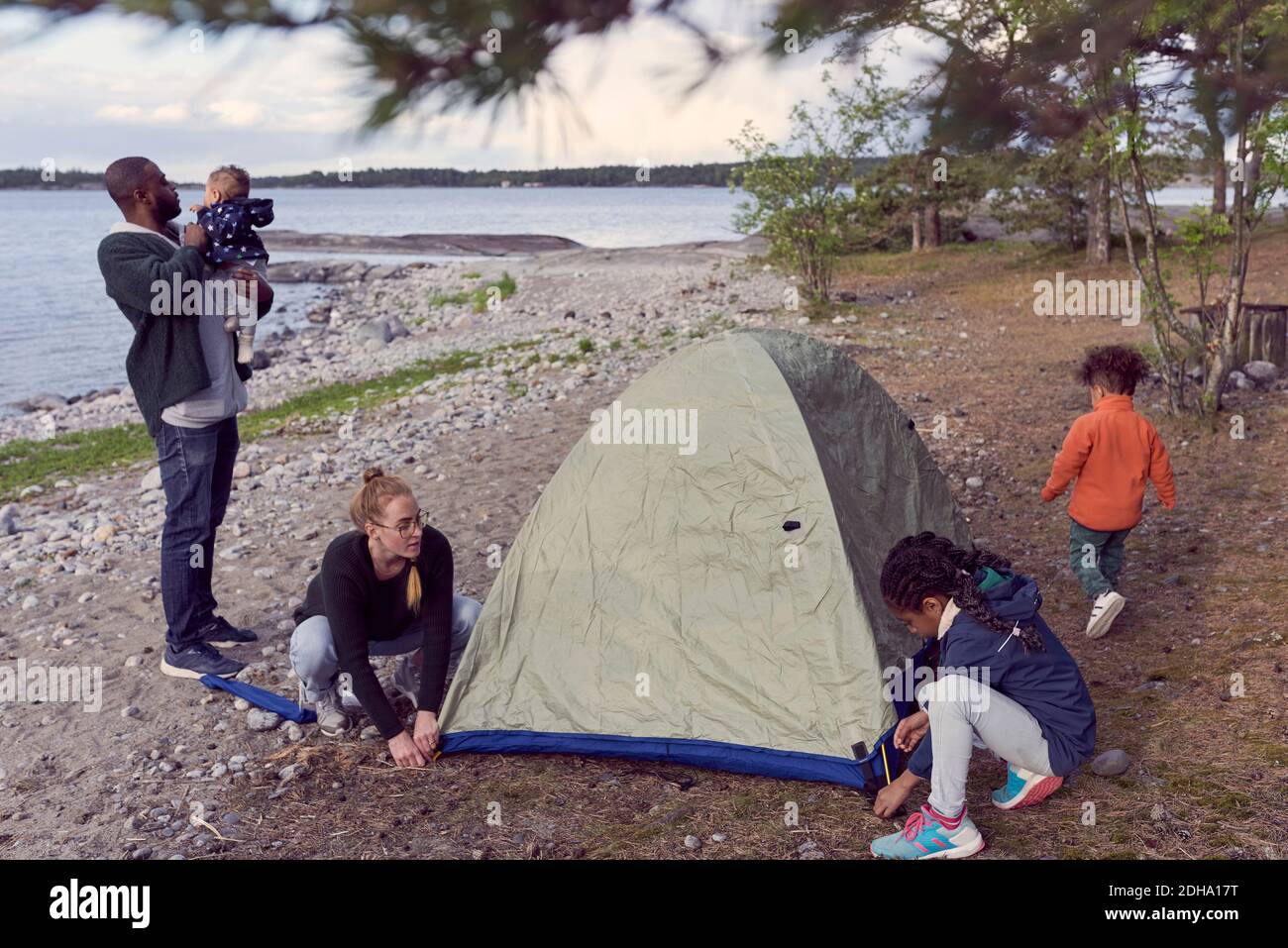 Padre che porta il bambino, mentre la donna e la figlia si accerchiano la tenda in spiaggia Foto Stock