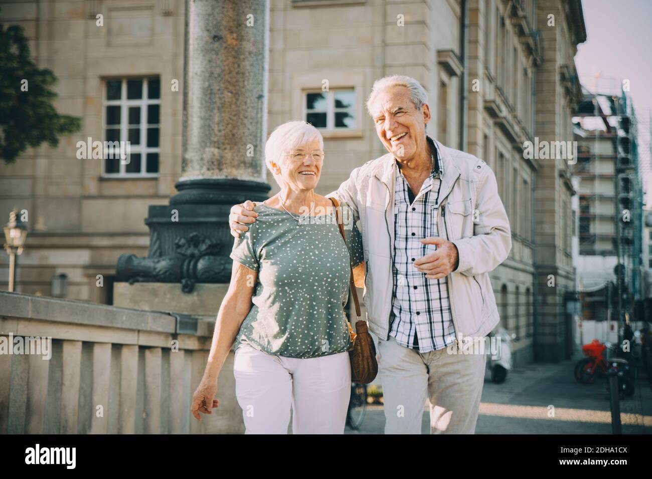 Uomo anziano sorridente braccio intorno a camminare con la donna in città il giorno di sole Foto Stock