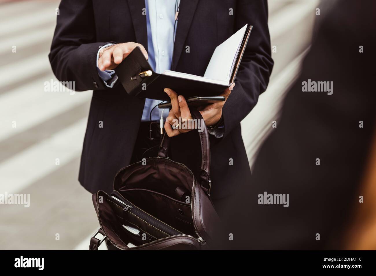 Sezione centrale della persona di affari maschile che tiene il libro mentre si levano in piedi all'aperto Foto Stock