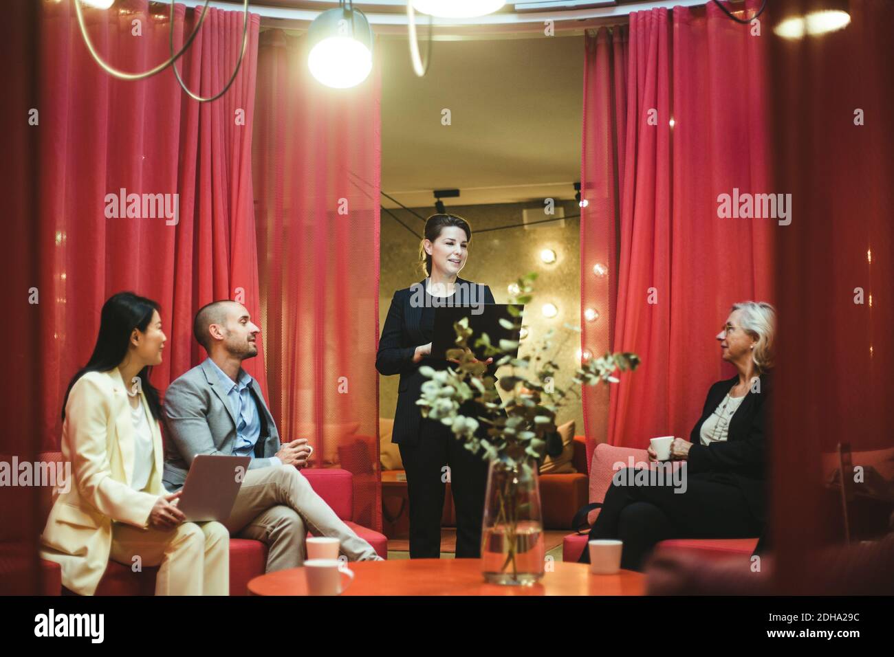 Dirigente femminile che tiene un computer portatile mentre discute le strategie aziendali con i colleghi in ufficio Foto Stock