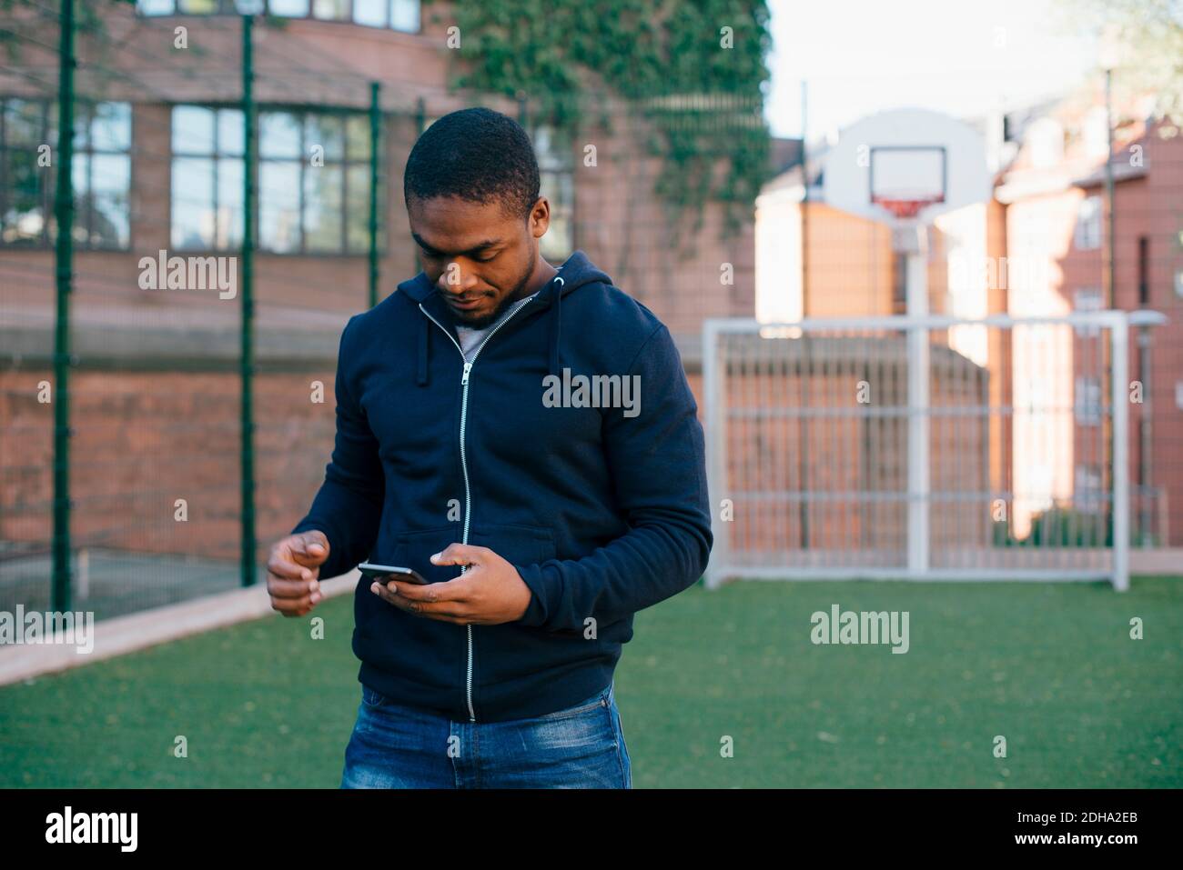 Giovane uomo in piedi sul campo da gioco mentre si usa lo smartphone Foto Stock