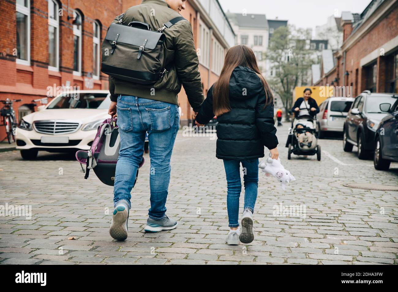Vista posteriore del padre e della figlia che tengono le mani che camminano sopra sentiero in città Foto Stock