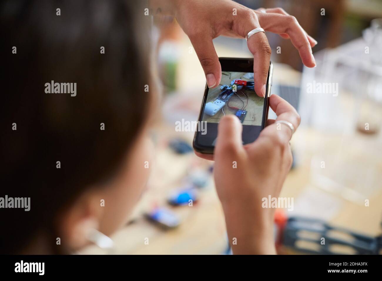 Immagine ritagliata di giovane ingegnere femminile che tocca lo schermo mobile mentre fotografare il modello in officina Foto Stock