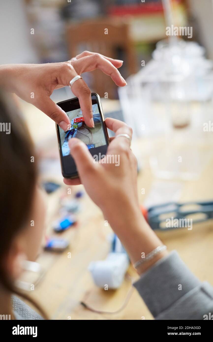 Immagine ritagliata di una giovane tecnico femminile che tocca lo schermo mobile mentre fotografare il modello sul tavolo in officina Foto Stock
