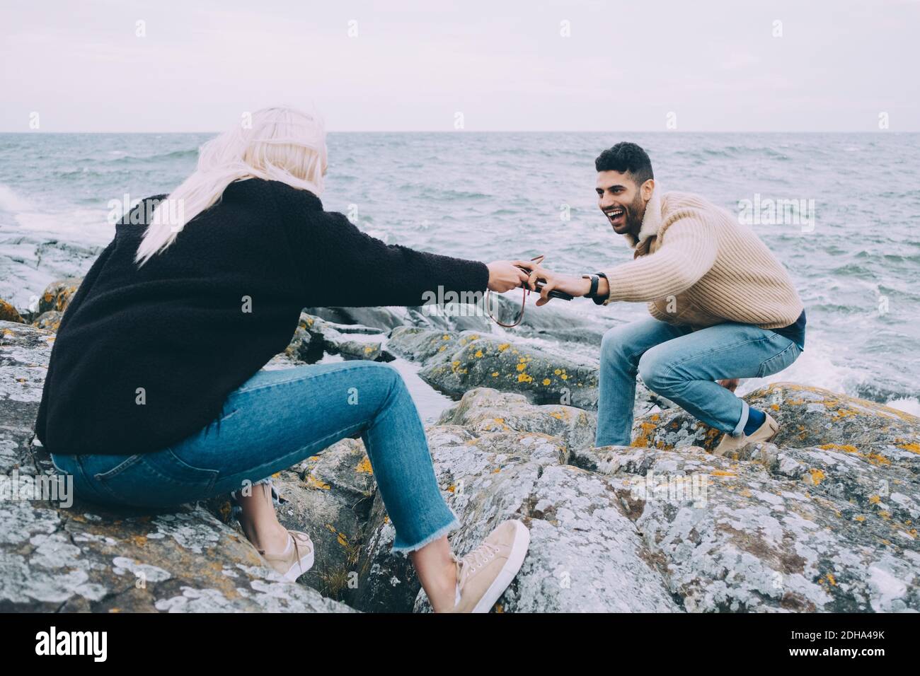 Giovane donna che passa telefono cellulare a uomo su rocce a. spiaggia Foto Stock