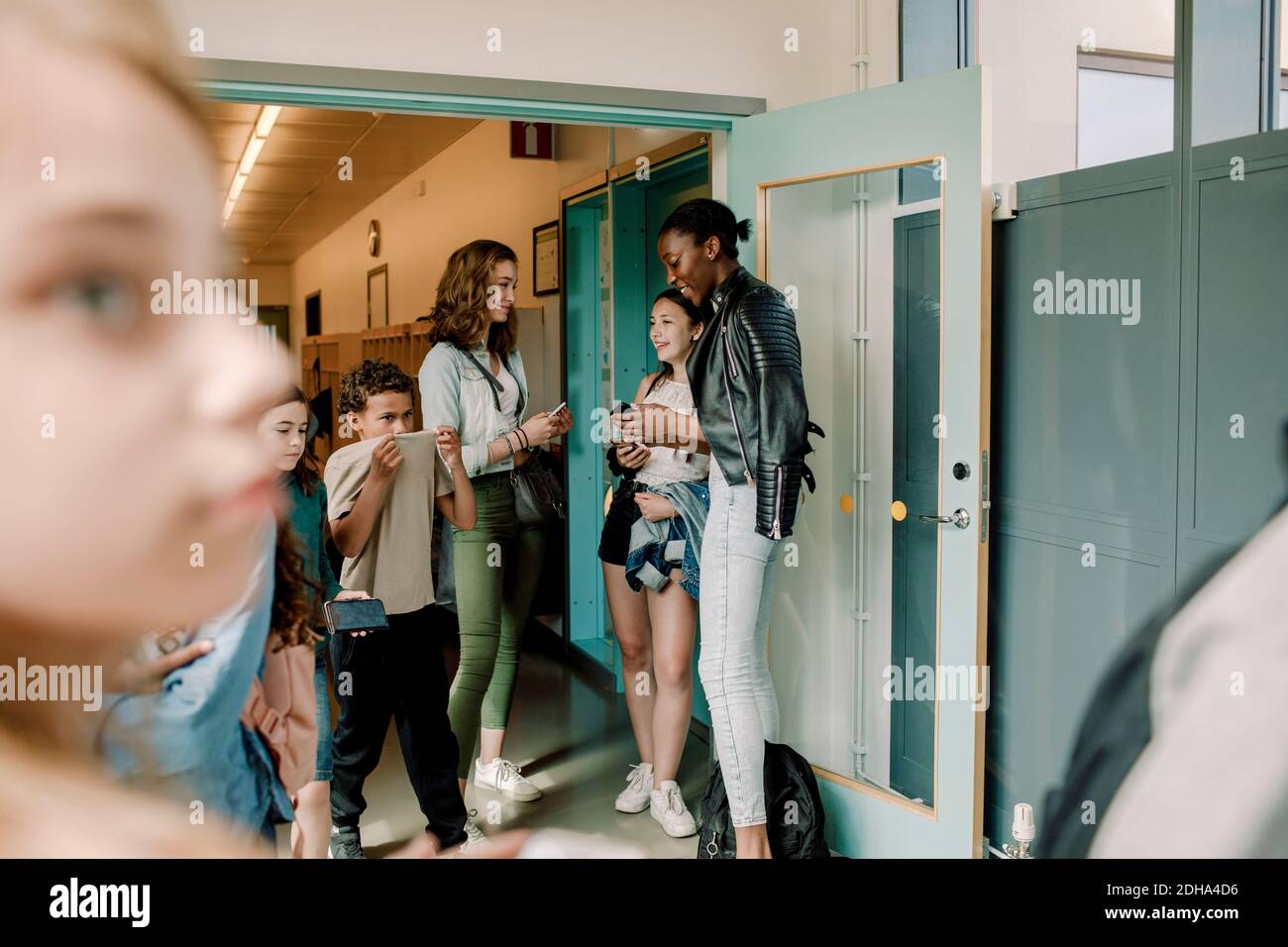 Studenti giovani sorridenti in piedi accanto alla porta nel corridoio scolastico Foto Stock