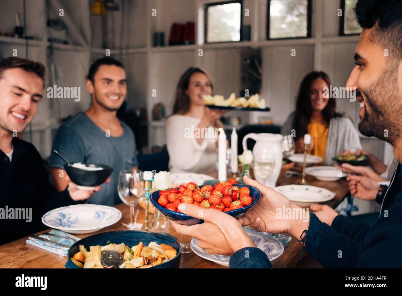 Giovane che tiene la ciotola di fragole seduto con gli amici per pranzo Foto Stock