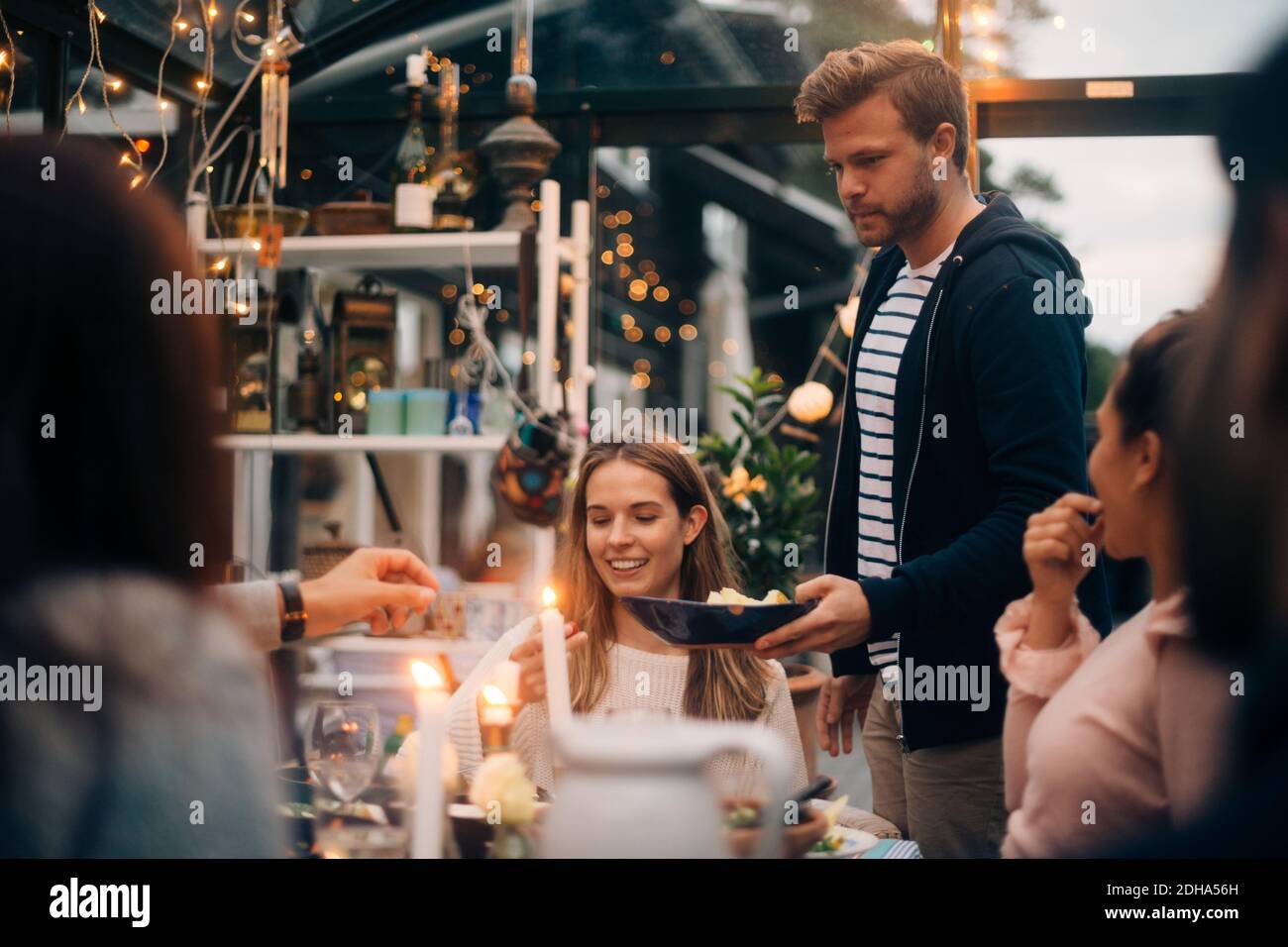 Giovane uomo che tiene un piatto di frutta mentre si alza in piedi da amici cabina in vetro Foto Stock