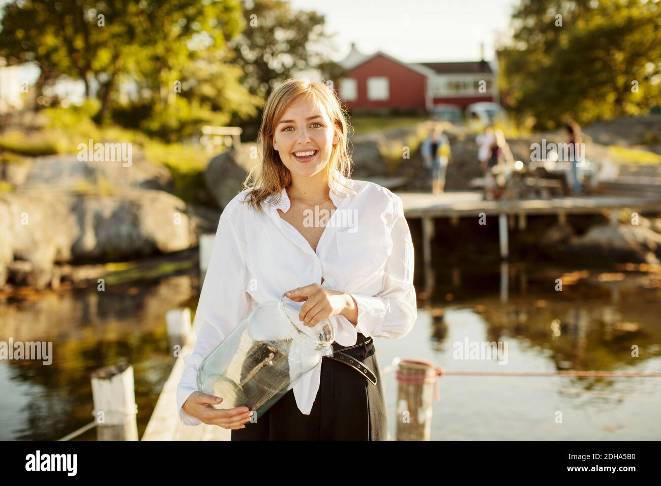 Ritratto di giovane donna sorridente che tiene il vaso in piedi sul molo al porto Foto Stock