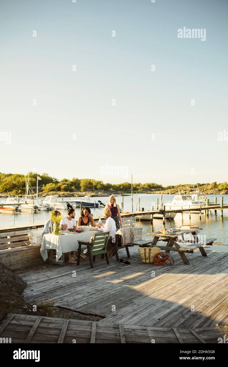 Gli amici gustano il pranzo al porto contro il cielo limpido sul sole giorno Foto Stock