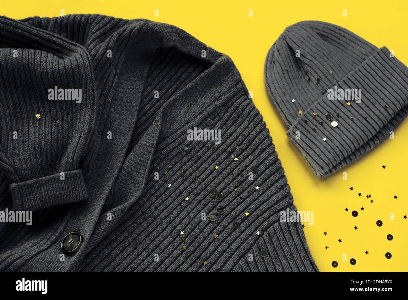 Pullover cardigan grigio e cappuccio su sfondo giallo con confetti. Colori alla moda dell'anno 2021. Vista dall'alto, disposizione piatta. Foto Stock