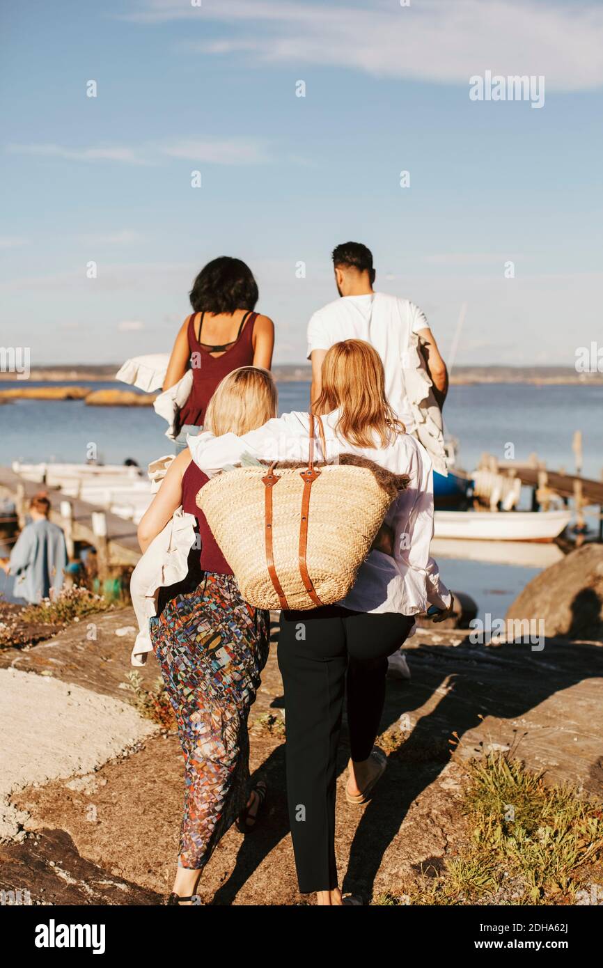 Vista posteriore degli amici che camminano verso il porto per una festa contro cielo Foto Stock
